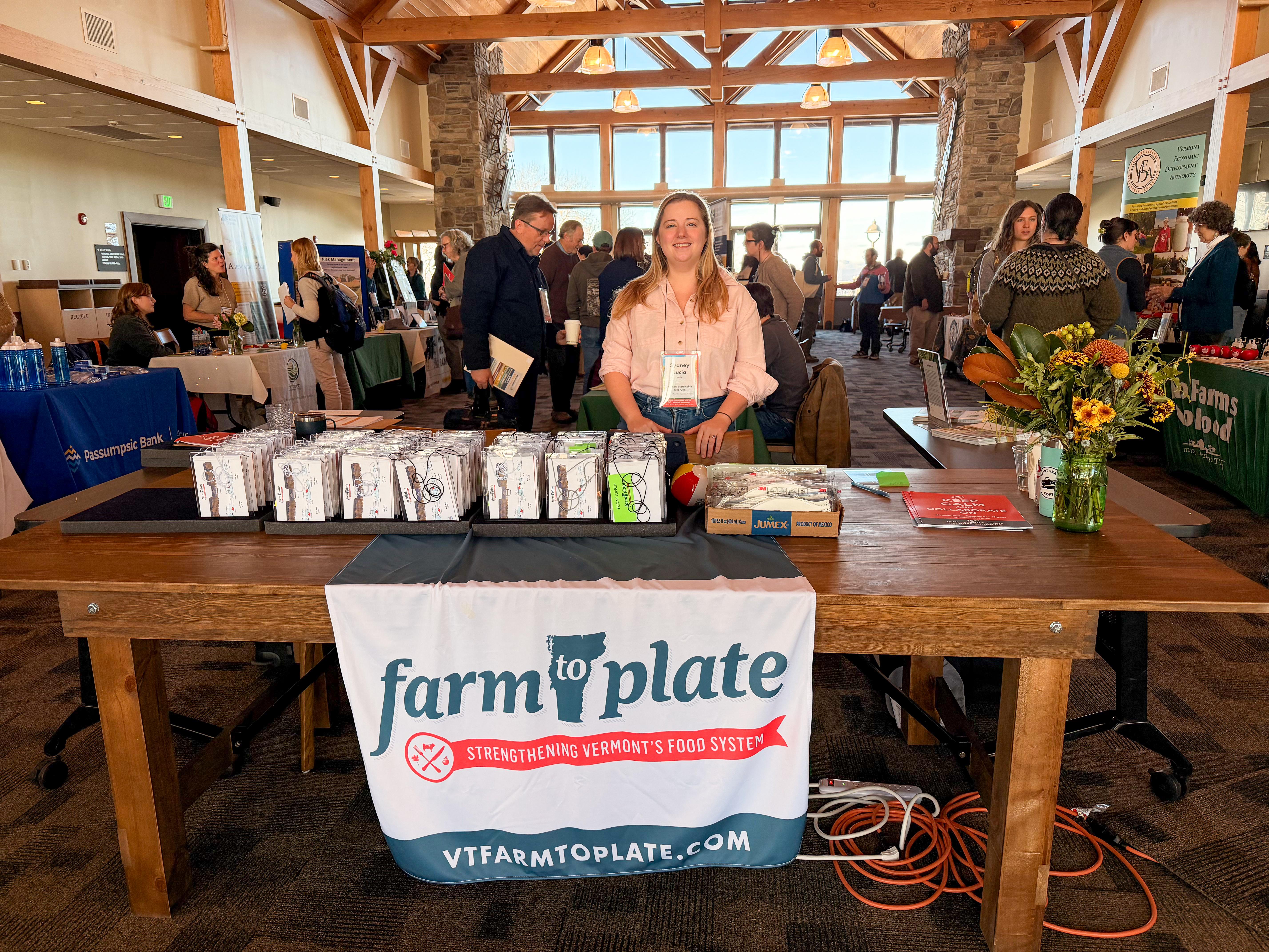 Sign in table at 15th Annual Farm to Plate Gathering. A person stands in front of the table with a Farm to Plate Banner and name cards on the table.
