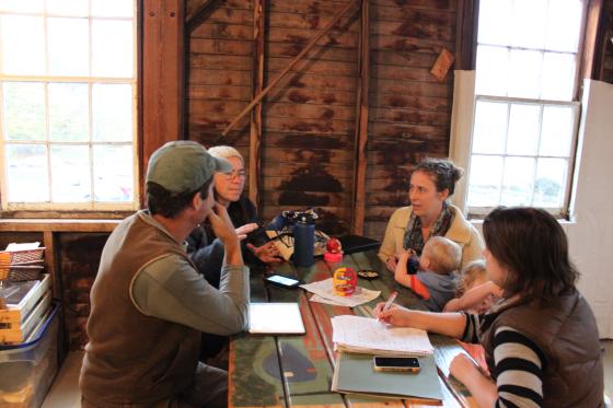 Four people sit at a wooden table, talking.