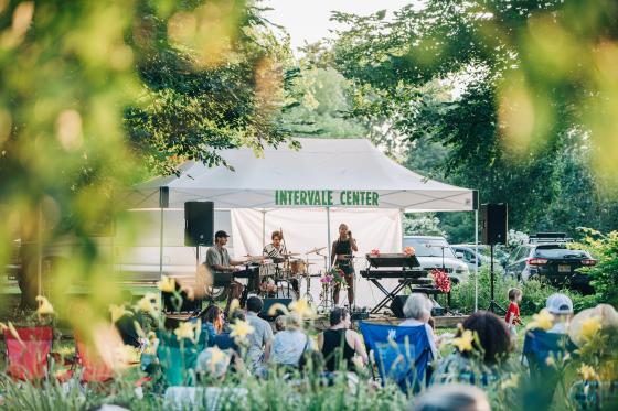 Band performing under a tent outside with audience members sitting in lawn chairs