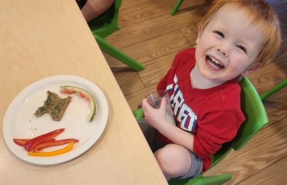 Child looking up and smiling with plate of fruits and vegetables