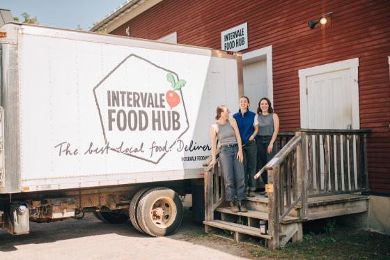 A box truck is backed up to a loading dock with three women standing next to the entrance